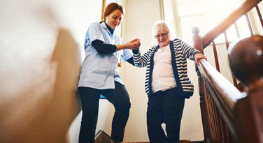 a caregiver helping an elder woman down stairs
